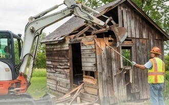 Excavator demolishing a small wooden shed